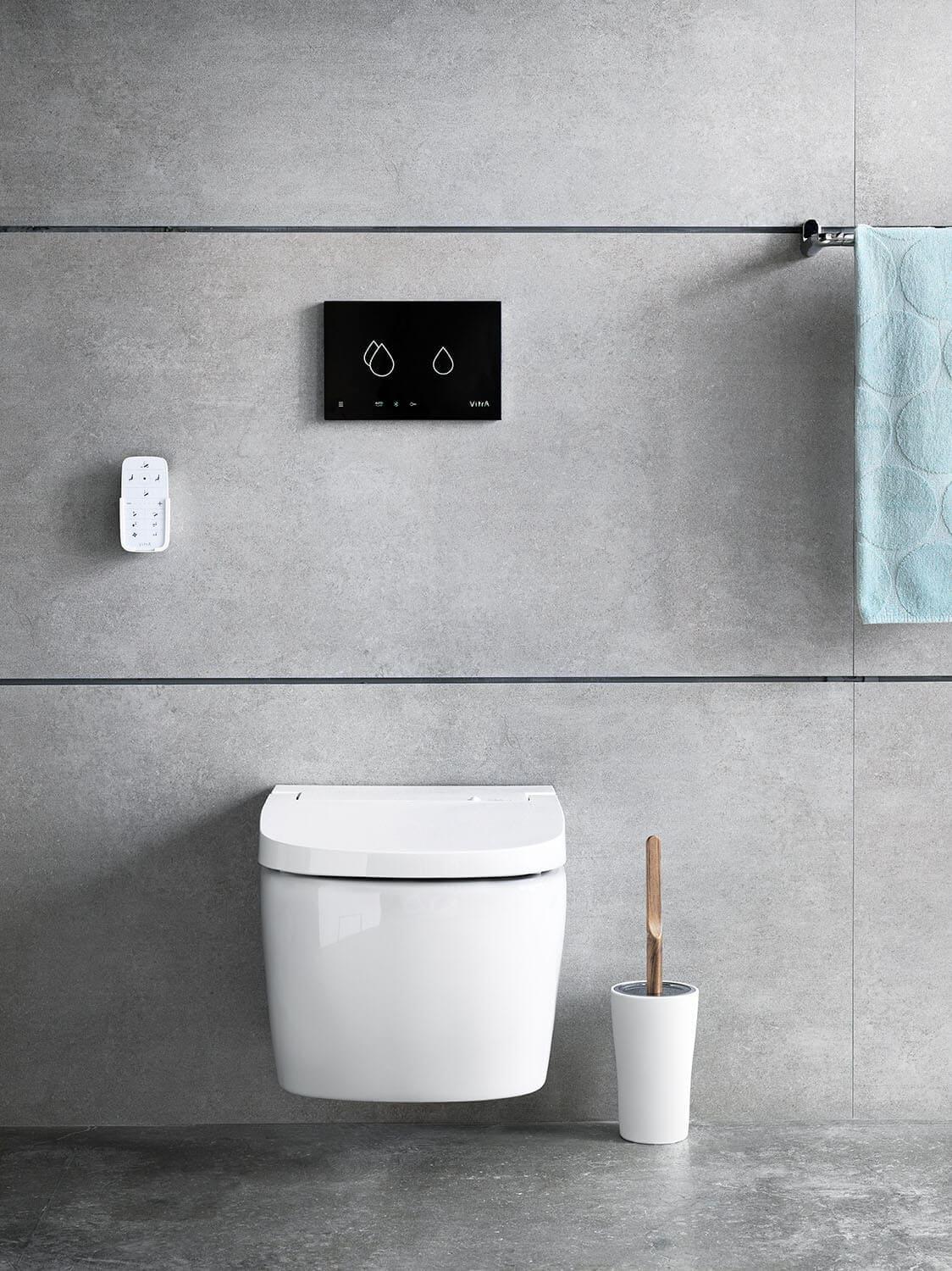 Weißes Dusch-WC vor grauer Betonoptik-Wand, rechts eine weiße Toilettenbürste mit Holzgriff.